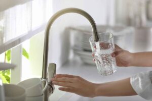 person (with a funny expression on their face) drinking water from the tap
