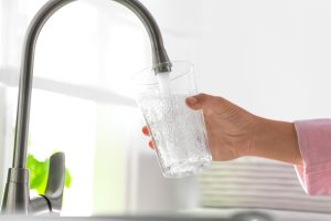 person filling a drinking glass with water from the tap